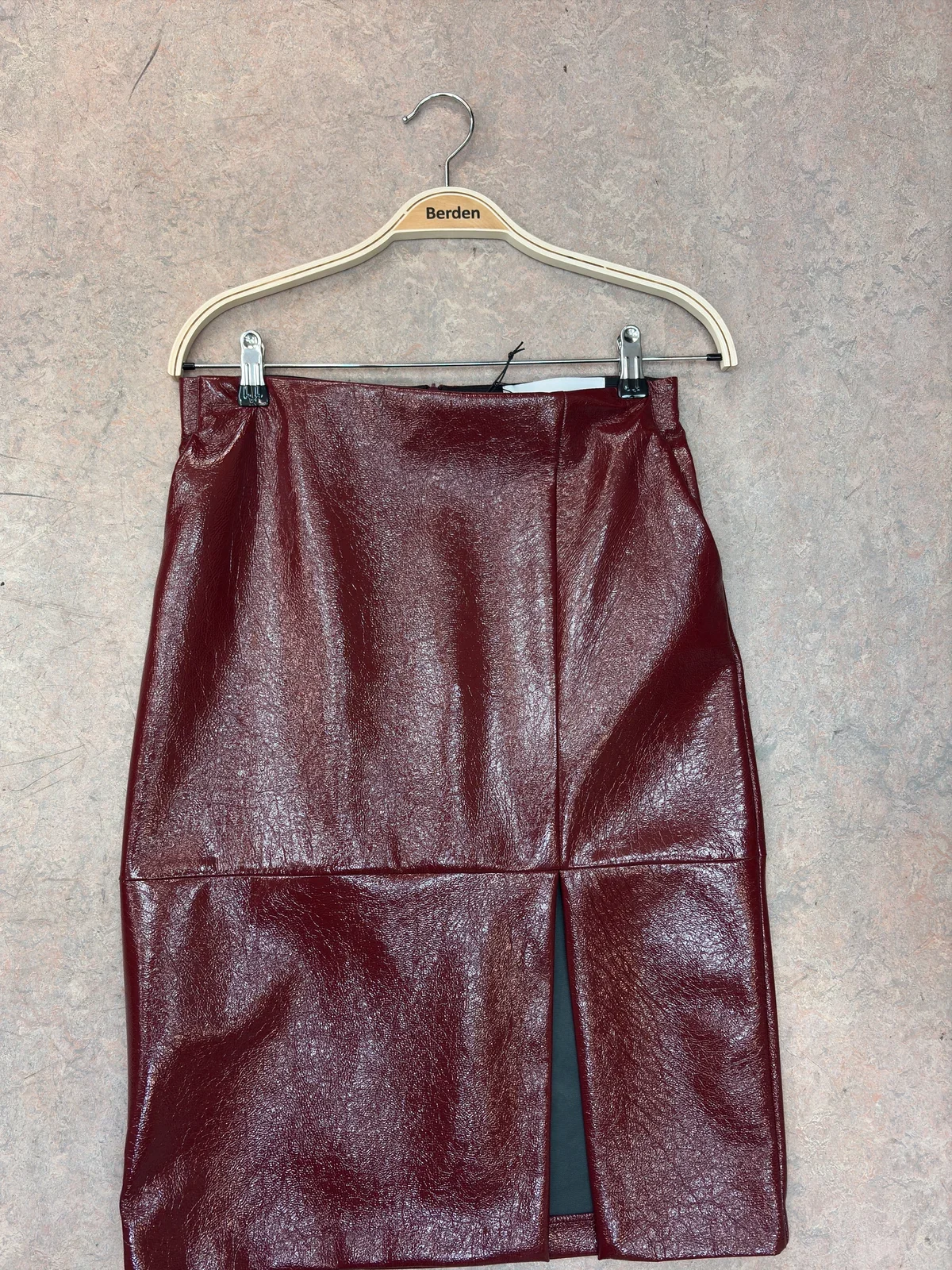 Burgundy patent leather skirt on a hanger, photographed on a concrete floor