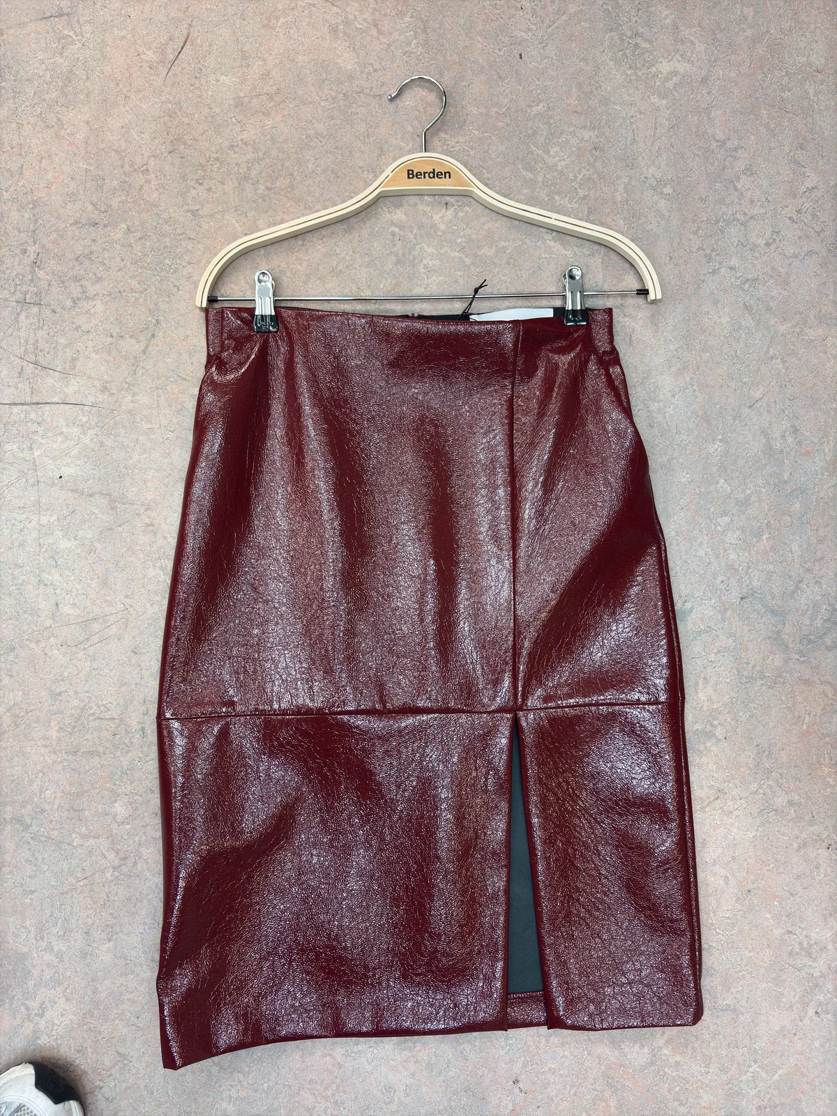 Burgundy patent skirt on a hanger, photographed on a concrete floor