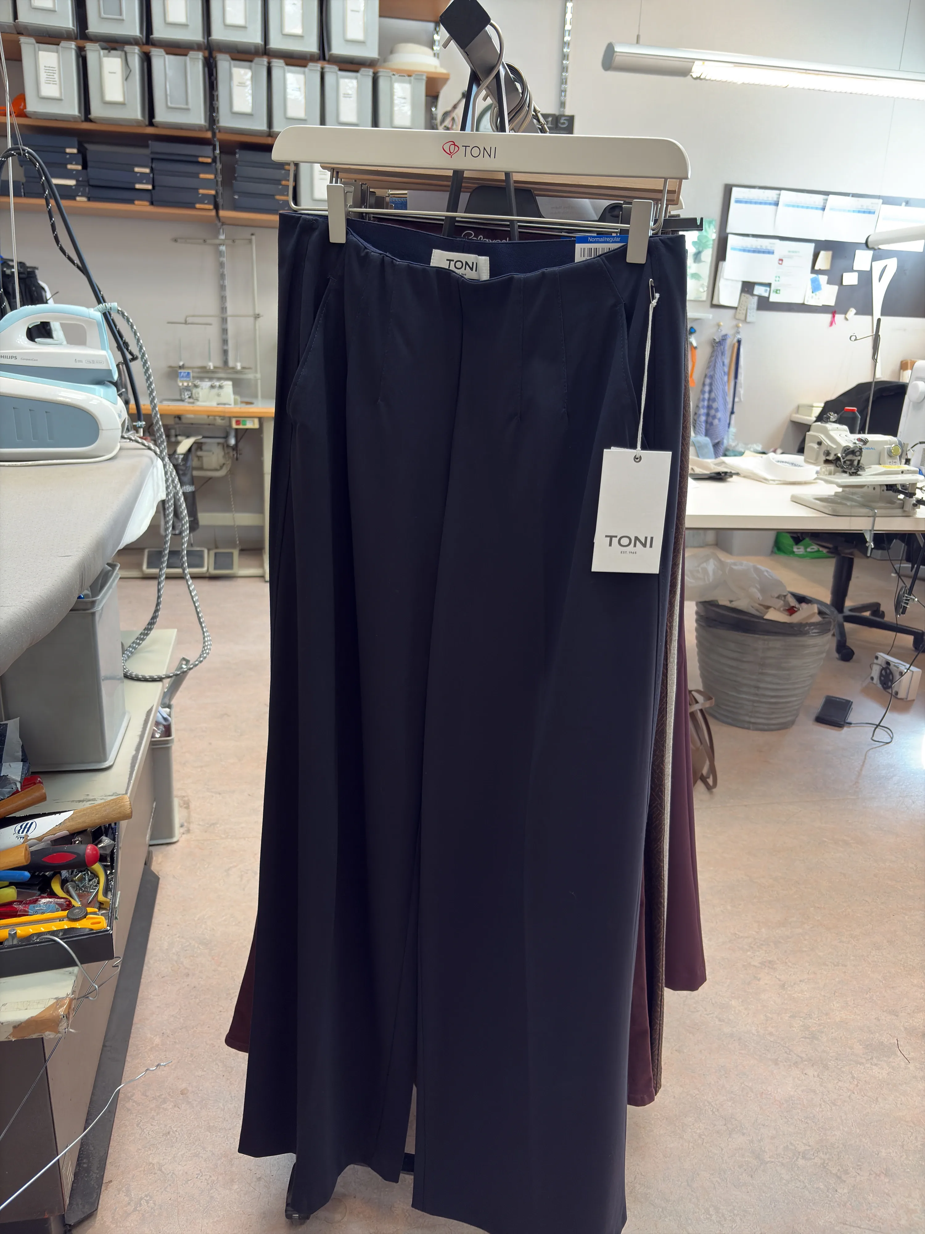 Navy blue trousers on a clothing rack in the studio, photographed with a phone