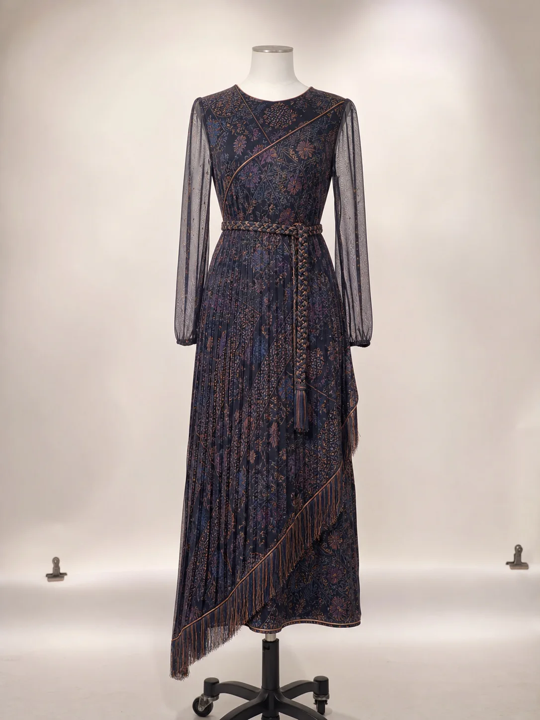 Dark pleated dress with fringe on a mannequin against a light studio background