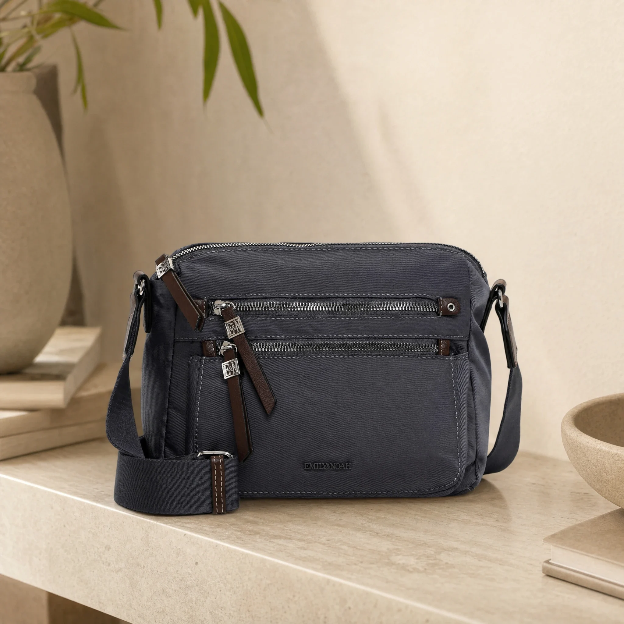 AI-scen: grå Emily & Noah-crossbody på ett ljust stenbord