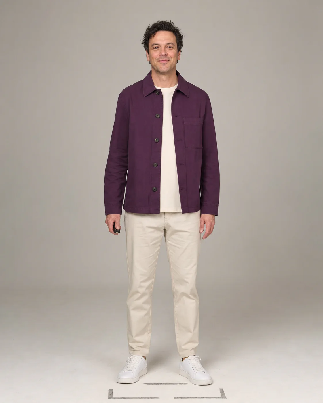 Studio shot of a man wearing a purple overshirt and light chinos, holding a remote control