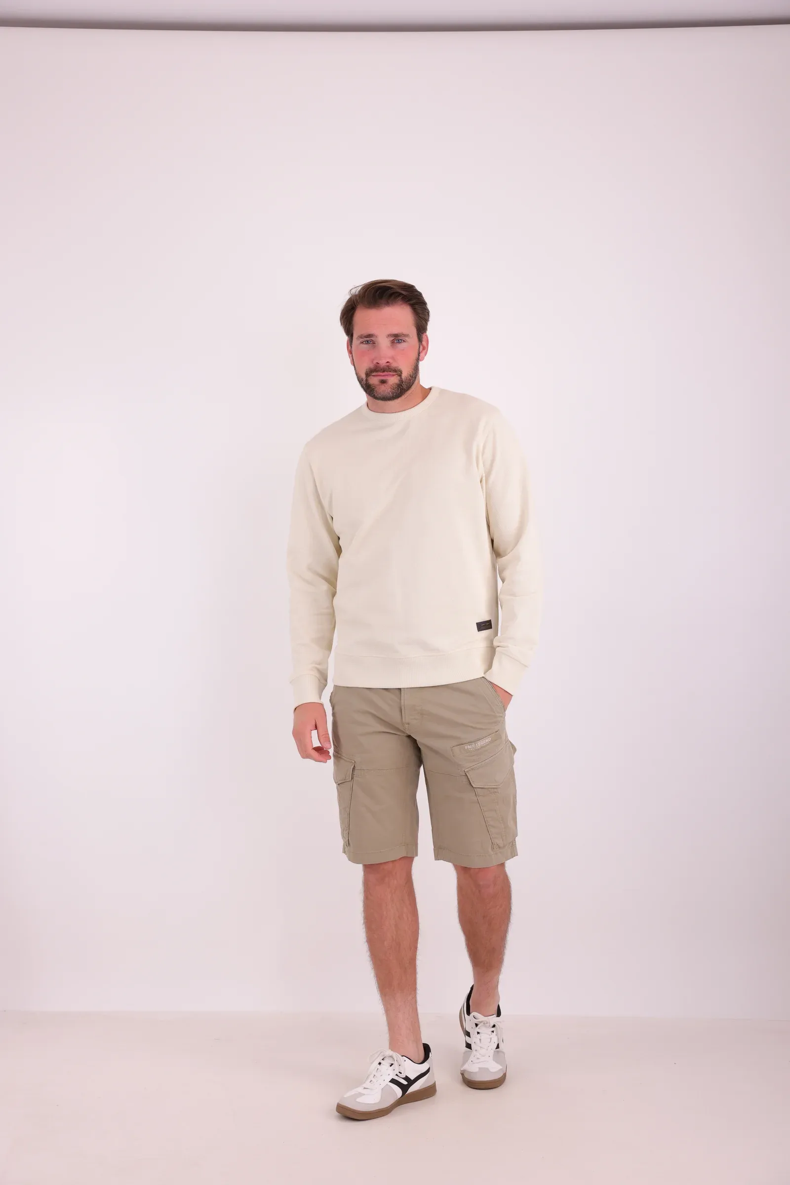 Studio photo of a model in a cream-colored sweater and beige cargo shorts